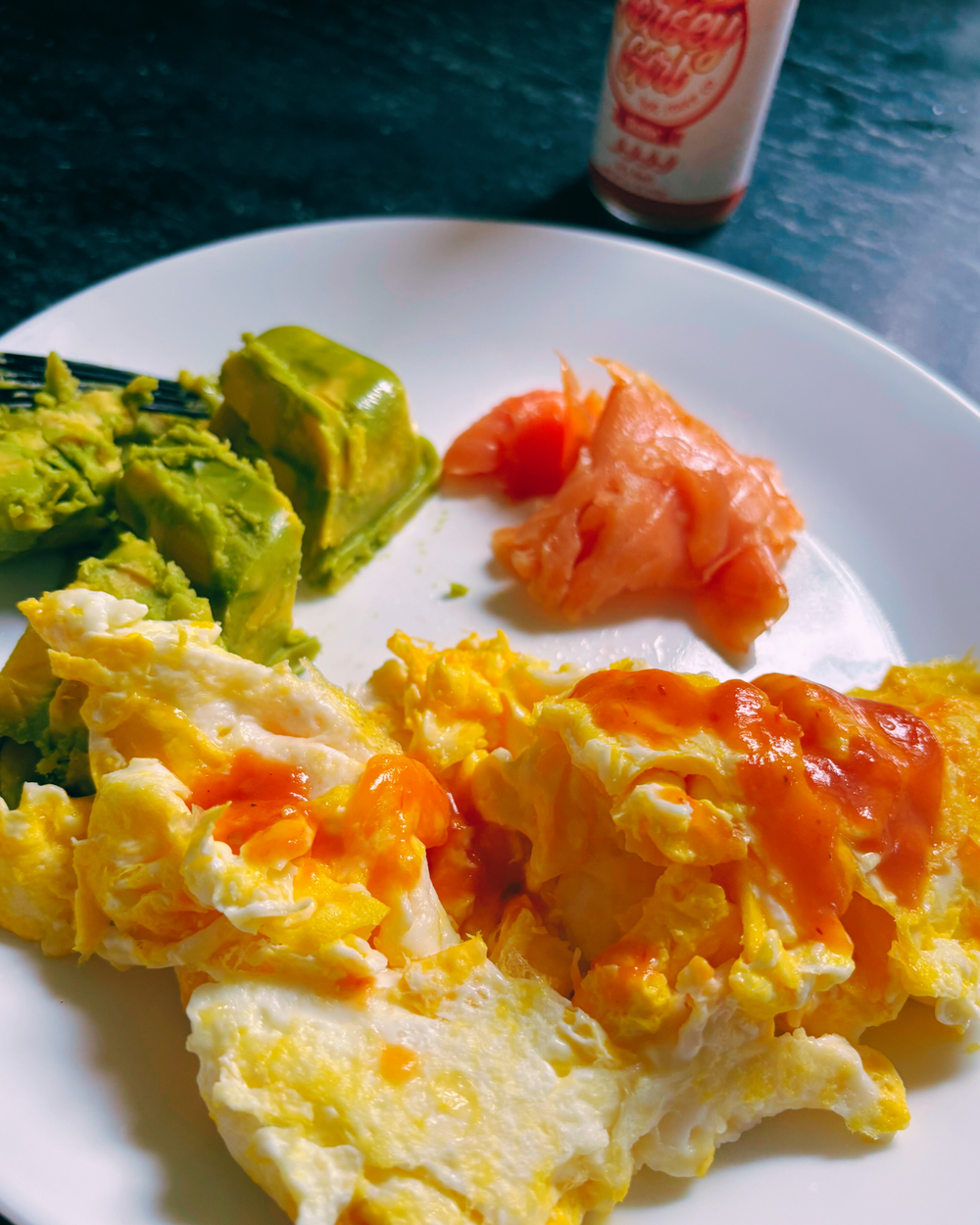 Plate with scrambled eggs, avocado, and salmon on a blue surface
