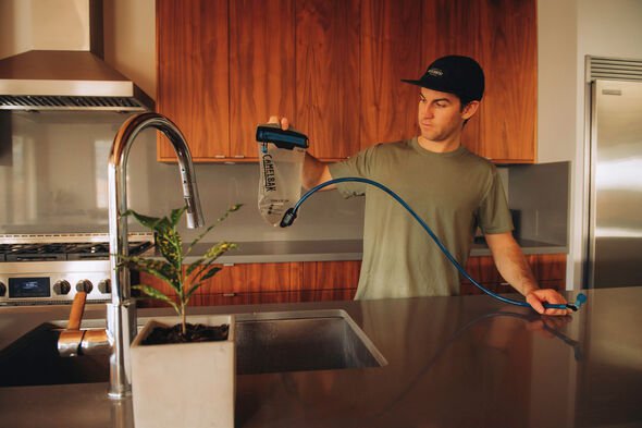 Man standing in a kitchen holding filled reservoir  with the  hose extended  